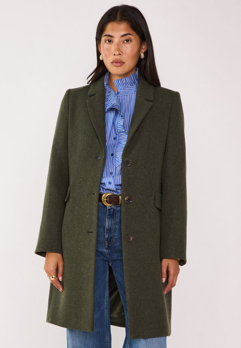 Cappotto di lana verde oliva con un design su misura, rever a scollatura, e tre bottoni. Presenta tasche laterali e un tessuto leggermente strutturato.