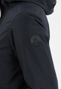 Giacca impermeabile navy con texture liscia, dotata di un patch rotondo nero sulla manica superiore che presenta grafiche di montagne e il nome del marchio.