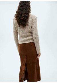 Beige, strukturiertes Sweatshirt mit langen Ärmeln, kombiniert mit einem braunen, Wildleder-Midikleid mit einem Schlitz hinten.