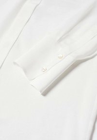 Gros plan sur le poignet d'une chemise blanche à manches longues avec deux petits boutons blancs sur un tissu lisse.