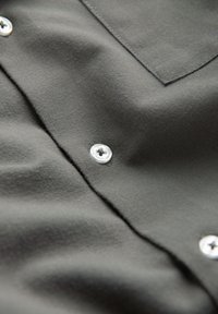 Gros plan sur un tissu gris foncé avec des boutons visibles et un coin de poche cousu.