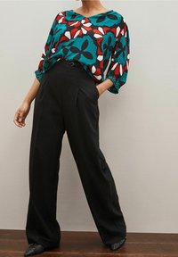 Blusa a fantasia floreale in teal, rosso e bianco abbinata a pantaloni neri a vita alta. La blusa ha una vestibilità ampia e maniche a tre quarti.