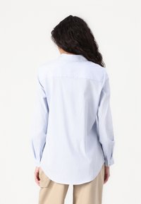 Cămașă cu dungi albastre deschise, cu nasturi, mâneci lungi, guler clasic, margine rotunjită și manșete cu un buton. Prezintă o croială lejeră.