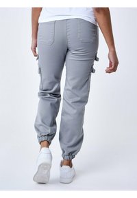 Grijze cargo pants met elastische boorden, voorzien van zijzakken en een getailleerd ontwerp. Draagt witte sneakers, gezien vanuit de achterkant.