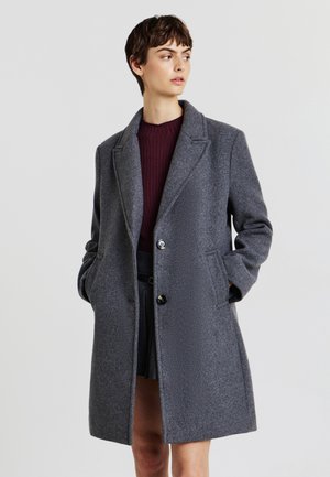 Cappotto grigio in lana con colletto a punta, chiusura con un bottone singolo e tasche laterali. Il tessuto ha una texture sottile e una finitura liscia.