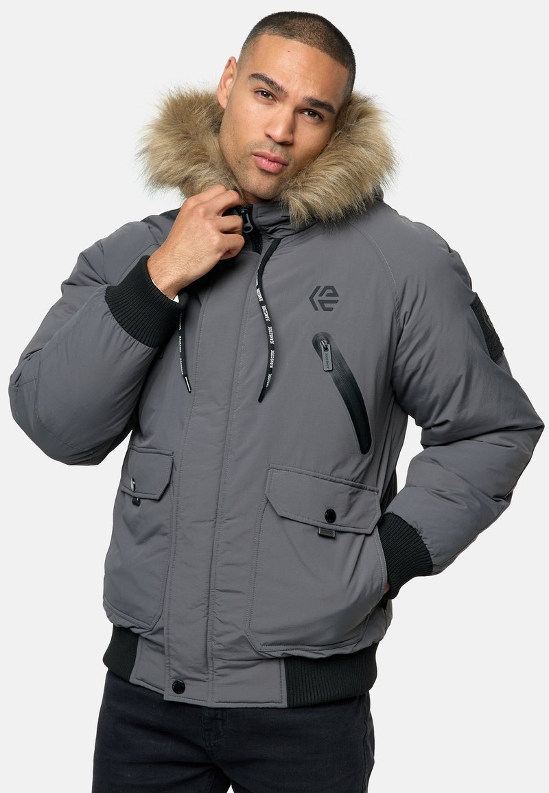 Graue isolierte Jacke mit einem gefütterten Kapuzenrand, Reißverschluss-Brusttasche, zwei frontalen Druckknopf-Taschen sowie gerippten Bündchen und Saum.