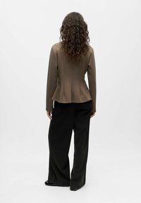 Rjav prilegajoč blazir s peplum silhueto, v kombinaciji z ohlapnimi črnimi hlačami. Tkanina se zdi gladka z nežno teksturo.