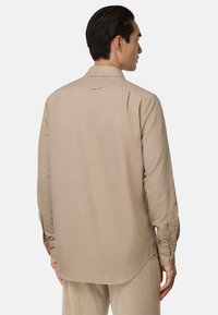 Beige herenoverhemd met lange mouwen, een klassieke kraag, achterste yoke en knoopmanchetten. De stof heeft een subtiele textuur. De zoom is rond.