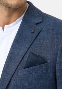Tumesinine kalasaba bleiser tekstuuriga viimistlusega, esitades rinnataskut, kus on tume tasku rúhet ja oranž nööp lapels.
