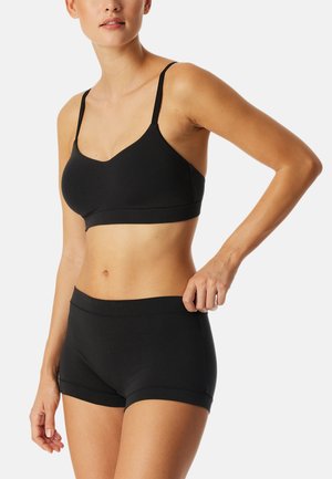 Bralette nera senza cuciture con spalline sottili e scollatura arrotondata, abbinata a short in vita alta coordinati, entrambi realizzati in un morbido tessuto elasticizzato.