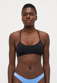 Svarte bikinitopper med tynne justerbare stropper, myk tekstur og minimalistisk design, kombinert med lyseblå bikiniunderdele.