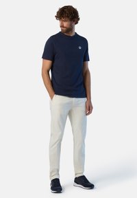 T-shirt di cotone blu navy con maniche corte e scollatura rotonda, abbinato a pantaloni aderenti beige e scarpe da ginnastica nere. Presenta un piccolo logo.