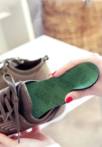 Brown athletic shoe with mesh and fabric upper, featuring a green removable insole marked with "ACTI CARBON" and pattern of perforations.