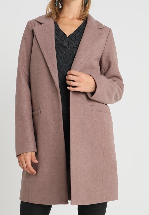 Lyserød, uldblanding frakke med skræddersyet design, spidse revers og sidelommer. Modellen har en sort sweater på under.