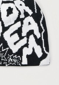 Μαύρος και άσπρος πλεκτός σκούφος με έντονα, αντίθετα κείμενα και γραφικά μοτίβα. Μαλακή υφή με εφαρμογή που αγκαλιάζει για ζεστασιά.