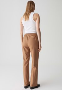 Pantaloni tailleur marroni con elastico in vita, caratterizzati da una texture morbida e un design a gamba dritta, abbinati a un top bianco senza maniche.