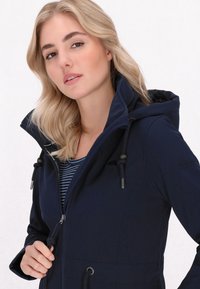 Giacca blu navy con cappuccio; presenta cordoncini, chiusura con zip e tasche. Indossata sopra una maglietta a righe, realizzata in un materiale liscio.