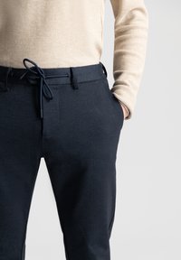 Navyblauwe broek van gestructureerde stof, met een koord taille, voorzakken en een relaxed fit, gepresenteerd met een beige langslavige top.