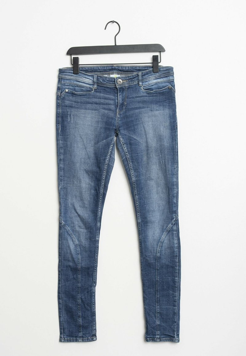 Strakke jeans gemaakt van blauwe denim met een vervaagde wassing, voorzien van steekzakken aan de voorkant, gebogen naden en een standaard tailleband, hangend aan een zwarte haak.
