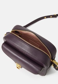 Borsa a tracolla in pelle viola con zip dorata, dotata di un vano principale e una tasca frontale. Texture liscia e branding sottile visibile.