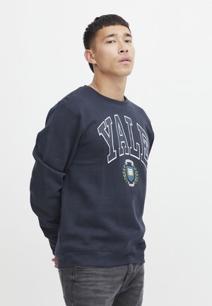 Navy sweatshirt with "YALE" in white letters, featuring a central graphic with a book and laurel leaves. Soft fabric, crew neck design.
