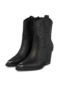 Botas de tobillo de cuero negro con punteras puntiagudas y acentos metálicos. Cuenta con costuras decorativas y un tacón apilado. Cierre de cremallera.
