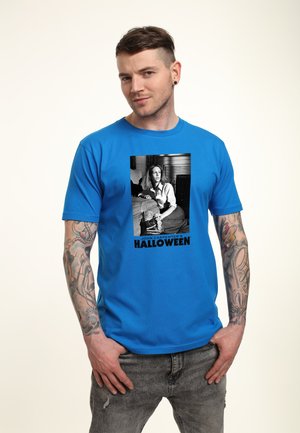 Blå bomulds t-shirt med en sort-hvid grafik af en kvinde med teksten "JOHN CARPENTER'S HALLOWEEN" under billedet.