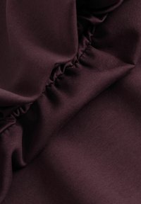 Gros plan d'un tissu violet foncé avec une couture élastique froncée créant de petites rides et plis.