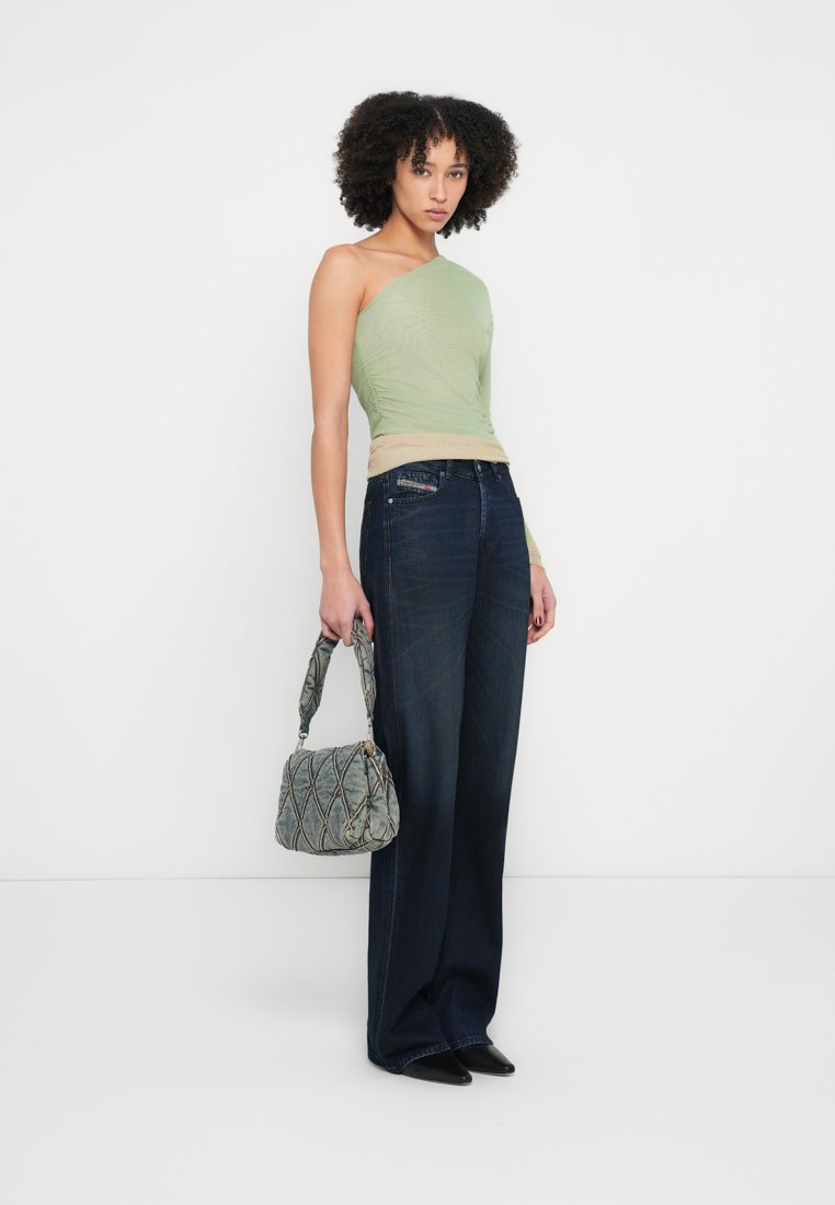 Haut asymétrique vert clair, bande beige à la taille, assorti à un jean large bleu foncé. Sac matelassé gris, chaussures noires à bout pointu.