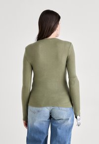 Olivenfarget langermet genser med en tettsittende design, myk tekstur og en lett buet hemline, kombinert med høyt liv blå denim jeans.