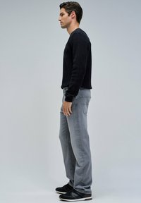 Suéter negro de manga larga, jeans rectos grises y zapatillas negras con suelas blancas. Diseños simples y texturizados; paleta de colores neutros.