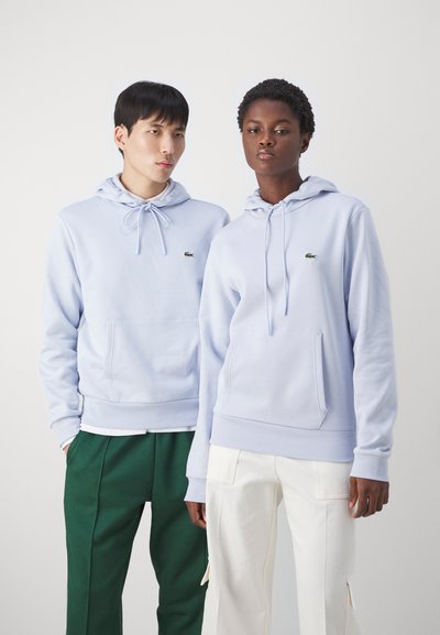 Sweatshirts bleu clair avec cordons de serrage, poches avant et petits logos. Associés à un pantalon vert et blanc, avec des plis et des poches.