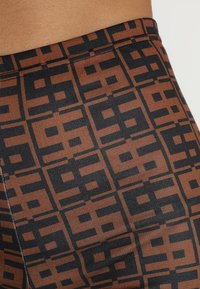 Brązowo-czarne legginsy z geometrycznym wzorem, wykonane z elastycznego materiału, o gładkiej fakturze i płaskich szwach.