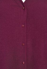 Bordeaux knoopshirt met een textuurstof, voorzien van een V-hals en vijf bijpassende knopen aan de voorkant.