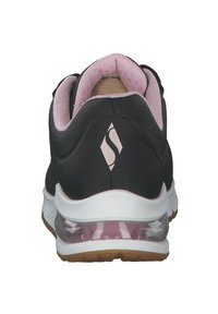 Zapatilla deportiva negra con un interior de malla rosa, cuello acolchado y amortiguación de aire clara en el talón. Presenta un logotipo sutil en la parte trasera.