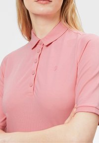 Polo rose avec manches courtes, col et patte de boutonnage à trois boutons. Fabriqué en tissu lisse et extensible avec un détail de logo subtil.