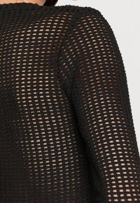 Vêtement tricoté noir avec un design en maille comportant des rangées de mailles ouvertes et fermées. Manches longues avec des détails texturés.