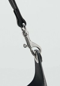 Fascia in pelle nera con un moschettone in argento metallico. La fascia presenta una superficie liscia e un design ad anello per il fissaggio.