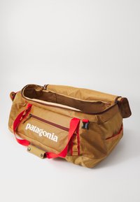 Brown Patagonia duffel bag with red handles and zippered compartments, open top showing spacious interior against plain white background.