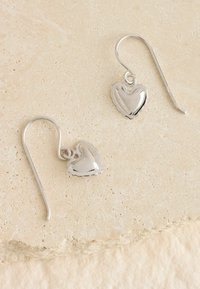 Srebrne kolczyki w kształcie serca z wypolerowaną powierzchnią i falistymi krawędziami, z zapięciem na haczyk dla zapewnienia bezpiecznego noszenia.