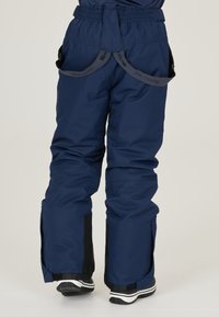 Marinblå snöbyxor med elastisk midja, justerbara axelremmar och svarta detaljer. Inkluderar blixtlåsförsedda sidöppningar för enkel på- och avtagning.