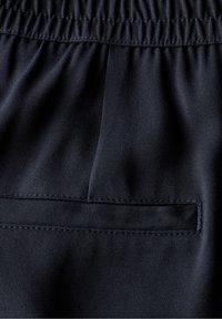 Tessuto blu navy scuro con una texture liscia. Presenta un cinturino elasticizzato e una piccola tasca inserita con un dettaglio di cucitura a taglio pulito.