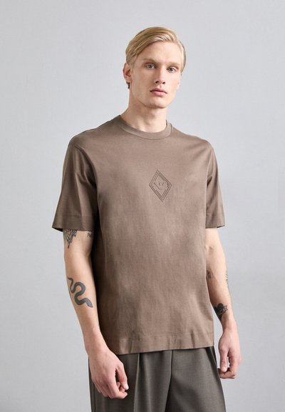 Tricou scurt, maro, cu maneci scurte, realizat dintr-un material moale, având un logo discret în formă de diamant pe piept și un design lejer.