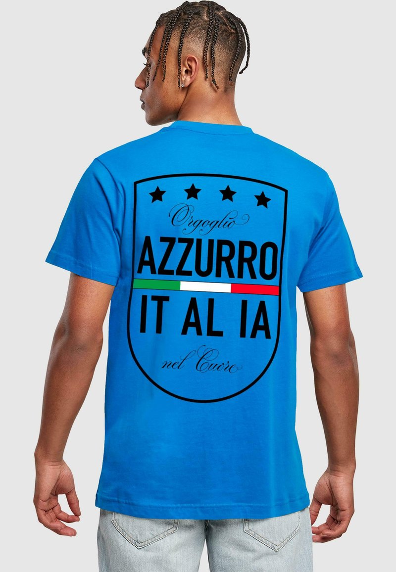 T-shirt in cotone blu con un grande design a forma di scudo nero sul retro, decorato con stelle, il testo "Orgoglio Azzurro IT AL IA" e accenti della bandiera italiana.