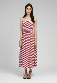 Robe maxi sans bretelles avec des rayures diagonales rouges et blanches, taille ajustée, jupe fluide et tissu léger. Sandales décontractées à lanière pour la cheville.