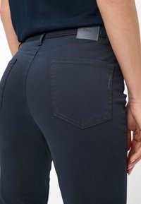 Dunkelblaue, dehnbare Baumwollhose mit schmaler Passform, ausgestattet mit zwei Gesäßtaschen und einem Leder-Logo-Patch am Bündchen.