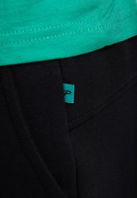 Grøn bomulds T-shirt over sorte strækbukser. Bukserne har et lille turkise mærke og en tekstureret stof med synlige sømme.