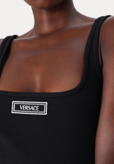 Top negru cu căptușeală, cu bretele late și decolteu pătrat, având un logo brodat alb "VERSACE" pe piept.