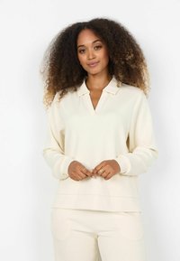 Pulover crem cu decolteu în V și guler, realizat dintr-un material moale. Mâneci lungi cu manșete, tiv stratificat și croială lejeră.