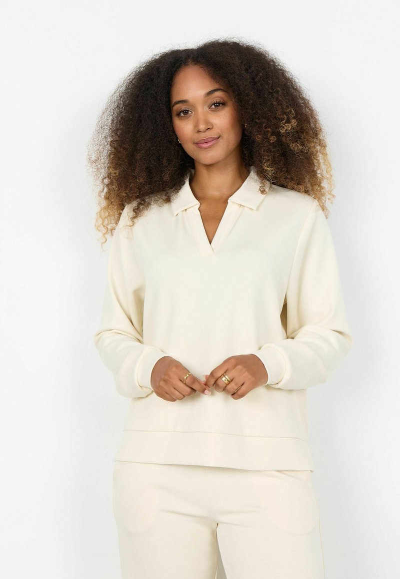 Pulover crem cu decolteu în V și guler, realizat dintr-un material moale. Mâneci lungi cu manșete, tiv stratificat și croială lejeră.